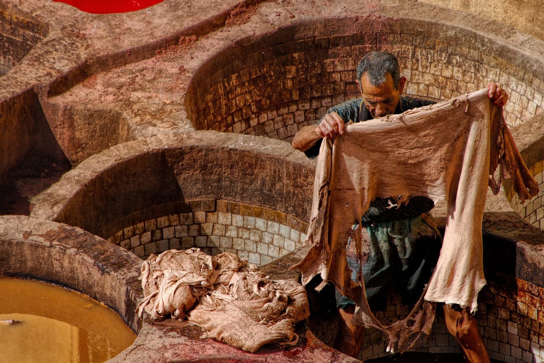 A leather worker holding a hide above traditional tanning pits