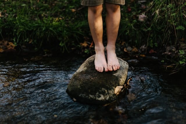 A person standing barefoot on a stone in flowing water